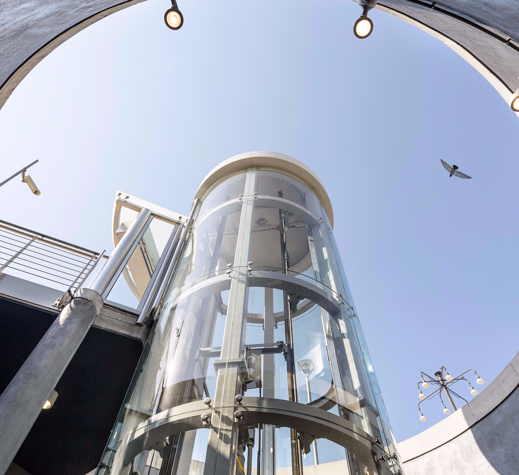 runder-aufzug-aussen-giotto a glass building with a railing and a body of water